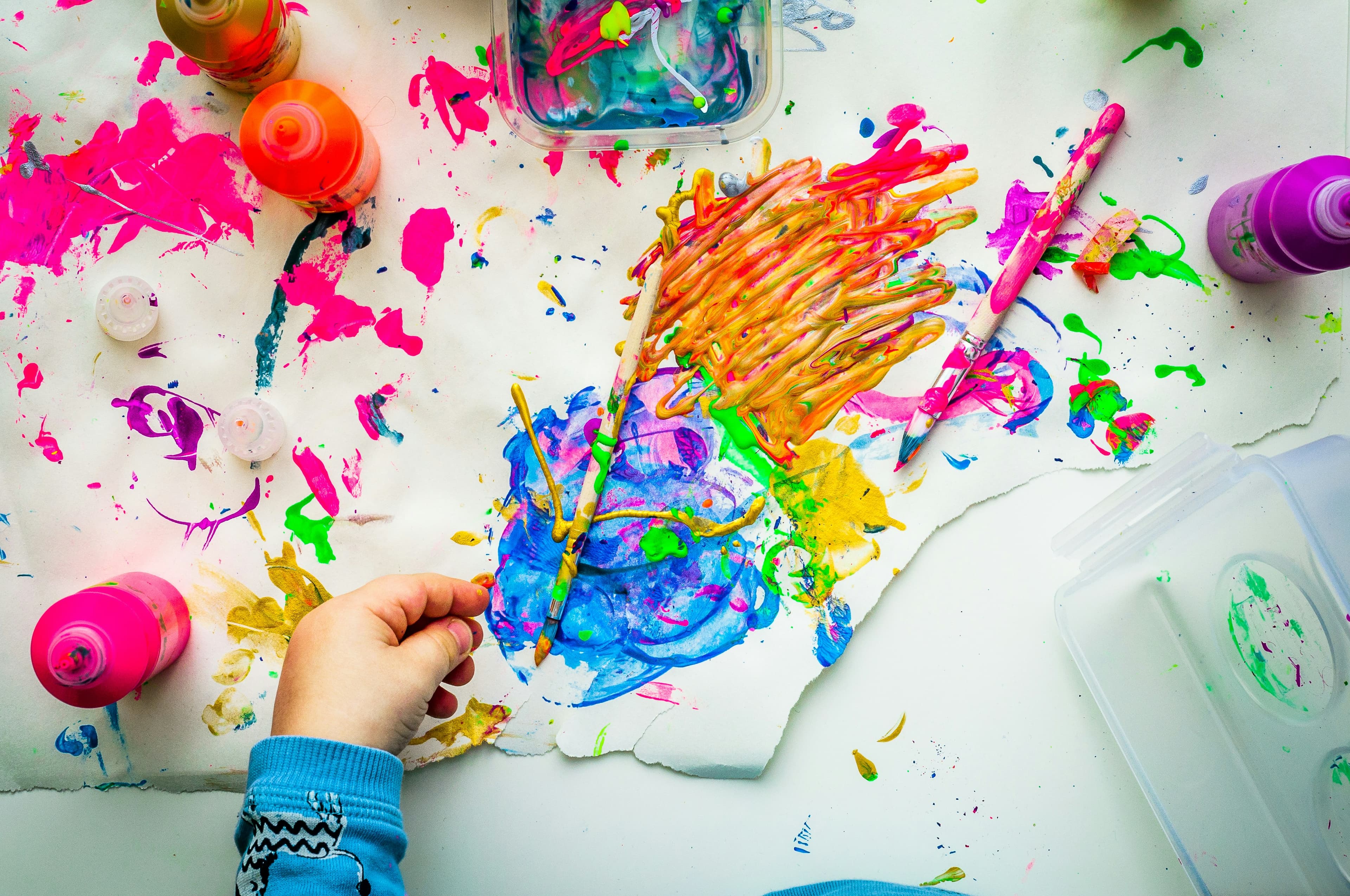 Une main d'enfant qui peint avec des couleurs vives, vue du dessus.
