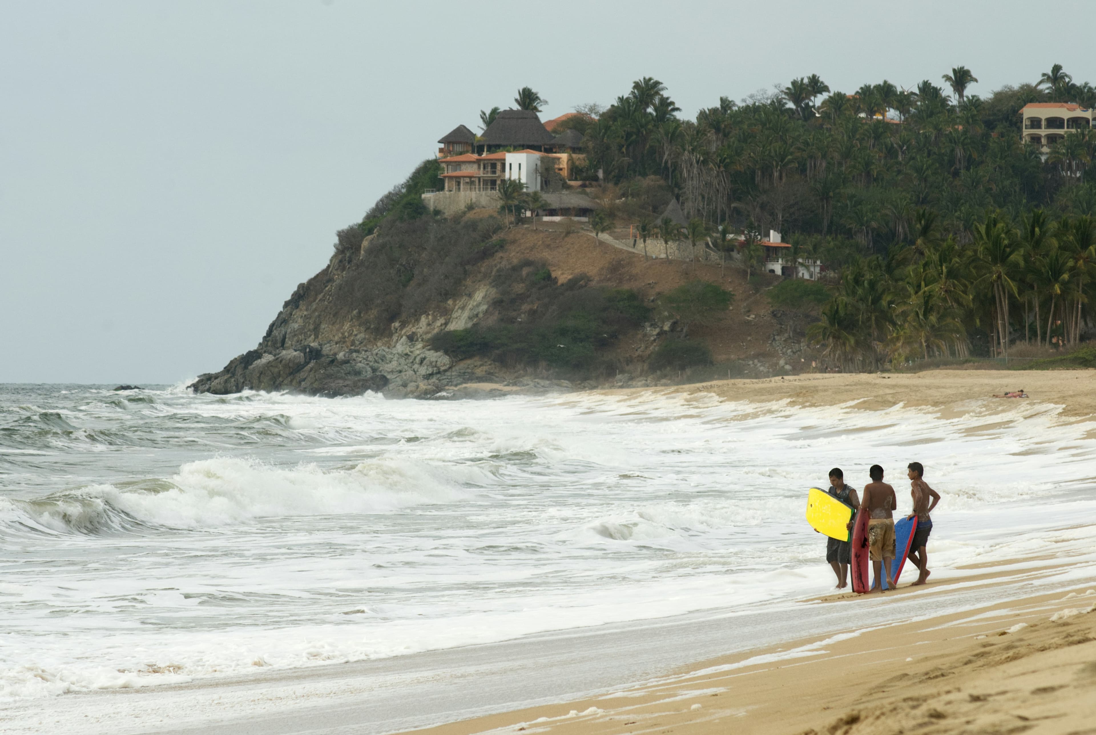 Trois personnes de dos avec des planches de bodyboard, au bord de l'océan.